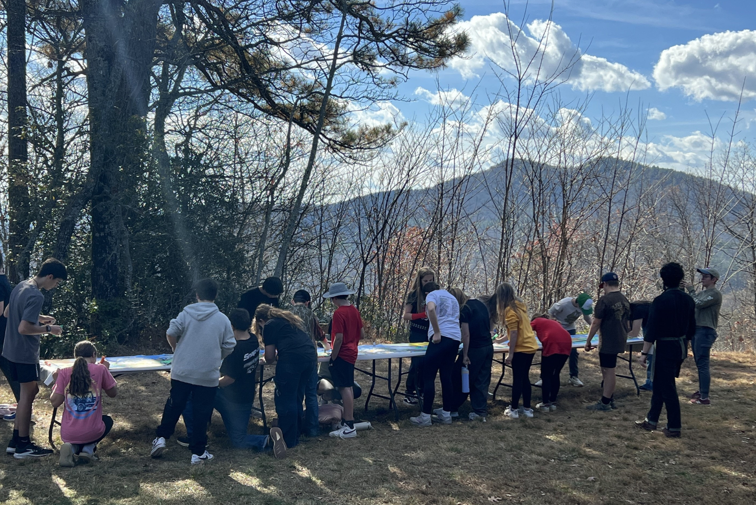 Students work around tables outside with the mountains in the distance.