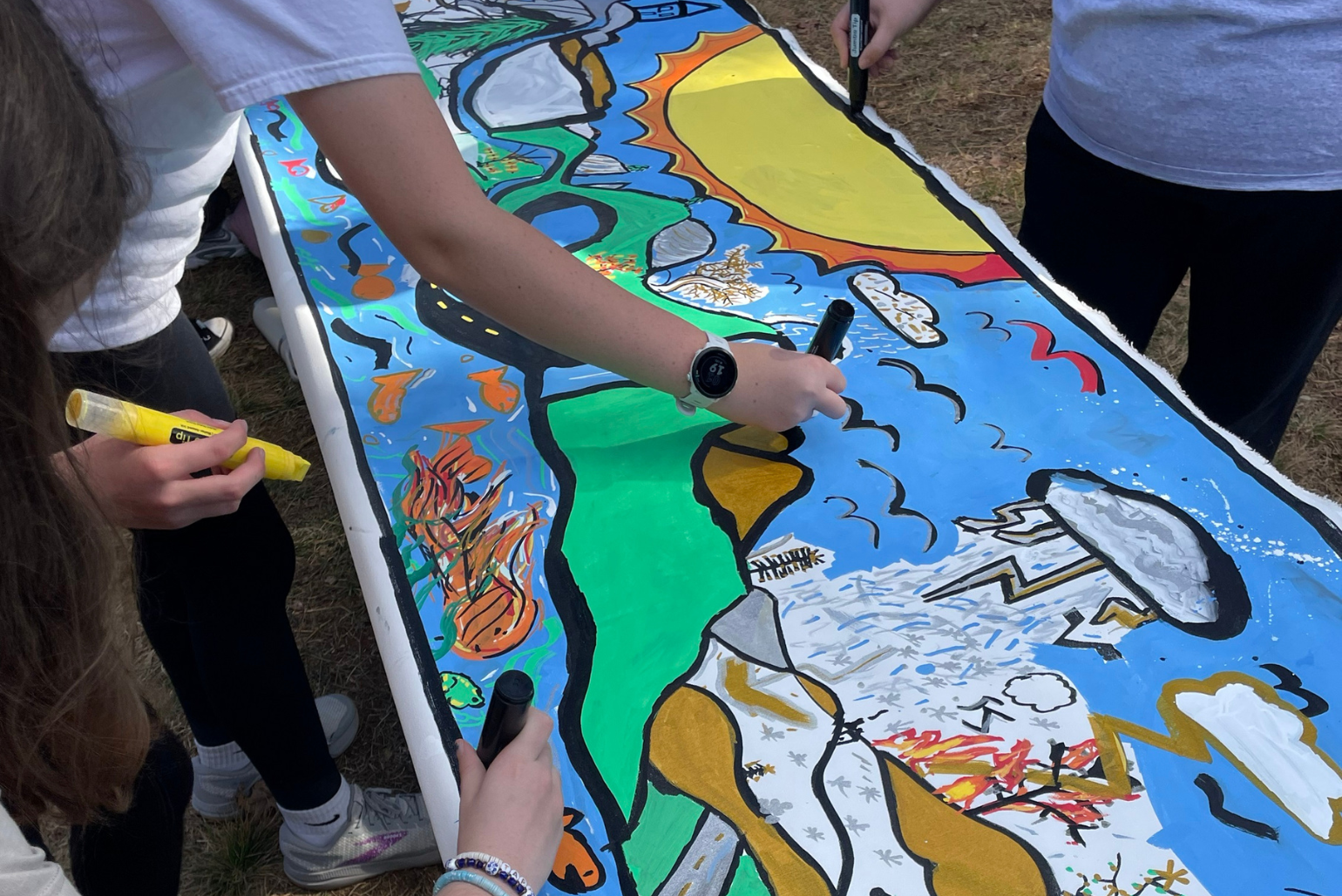 Students work on their mural by drawing storm clouds over the mountains.