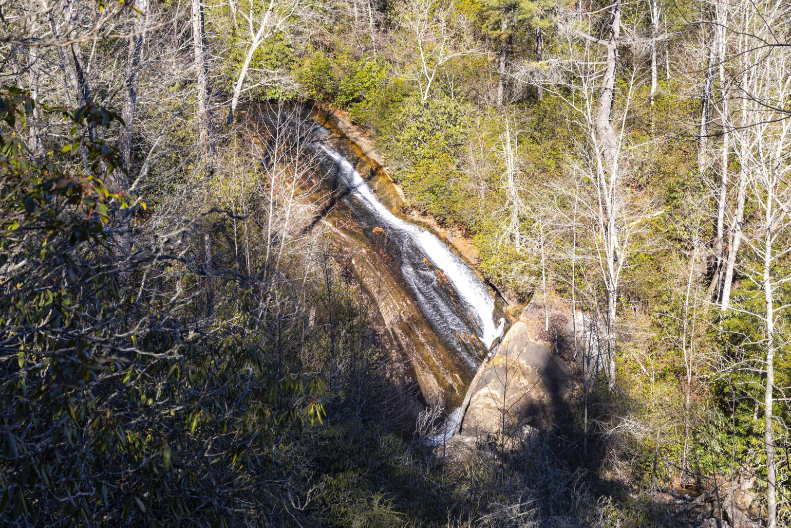 A waterfall cascades over brown rock with trees and other green vegetation surrounding it.
