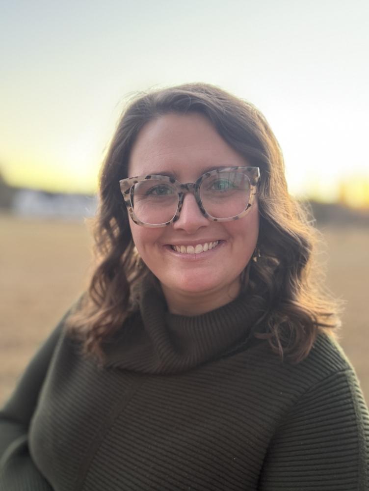 a white woman with shoulder length brown hair smiles in a green turtleneck