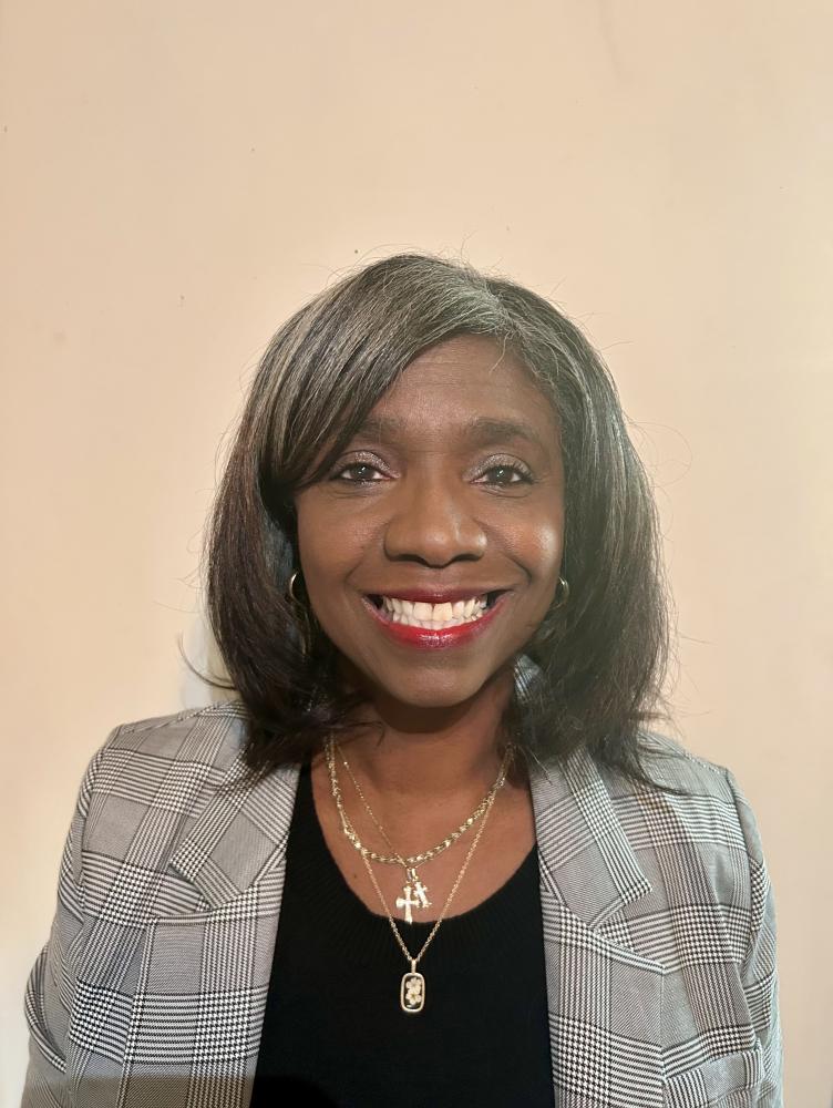 an African American woman with black hair and a gray jacket smiles at the camera