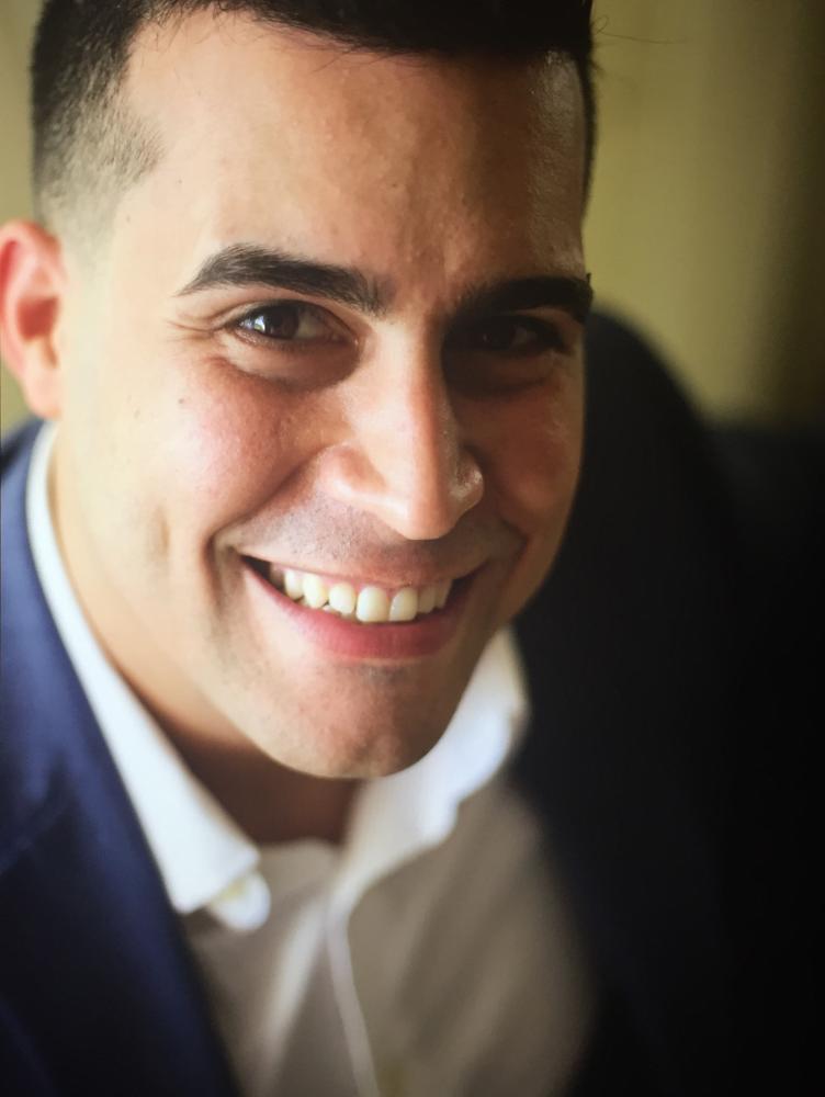 a man with black hair and a blue suit jacket smiles up at the camera