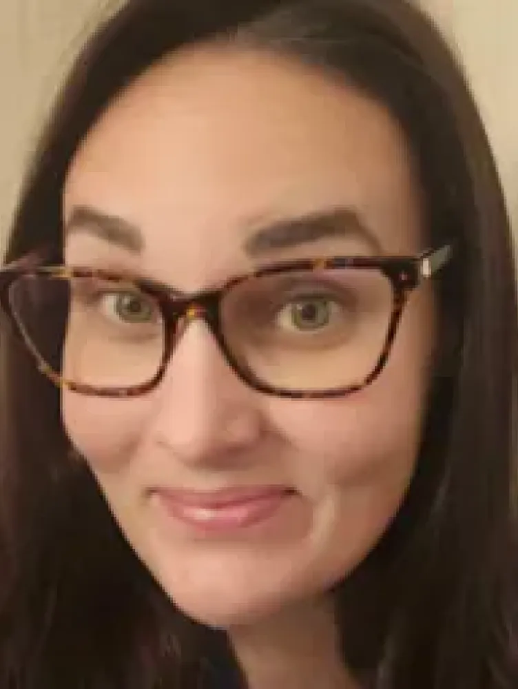 a woman with long dark hair and glasses smiles at the camera