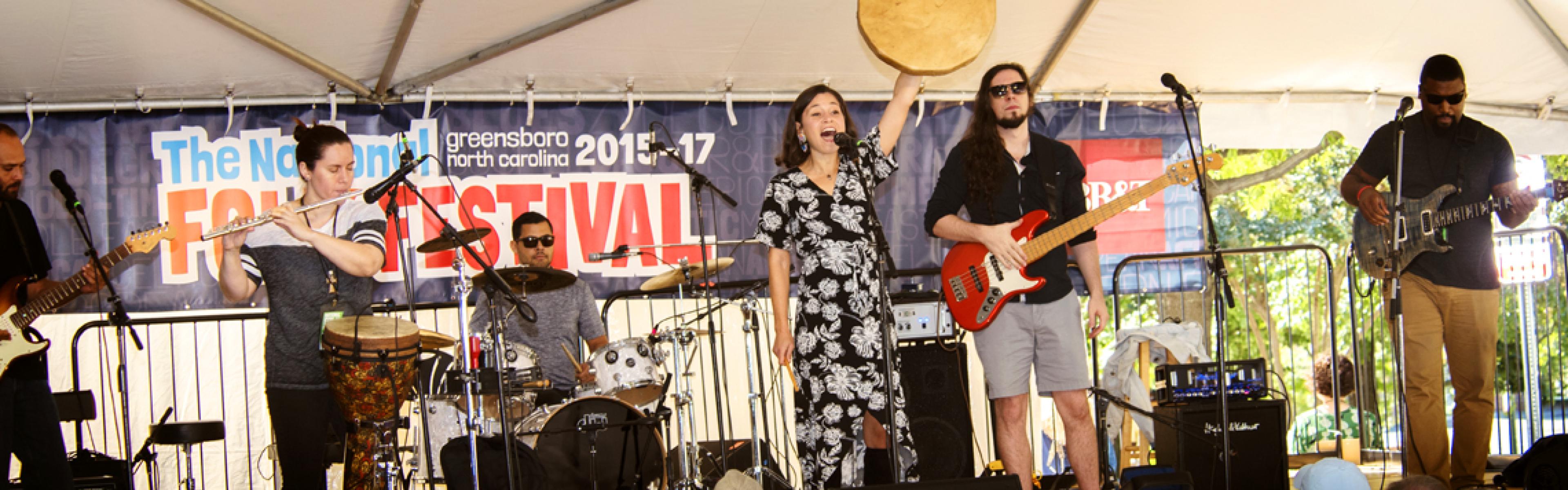 A band plays onstage in front of a crowd under a large tent