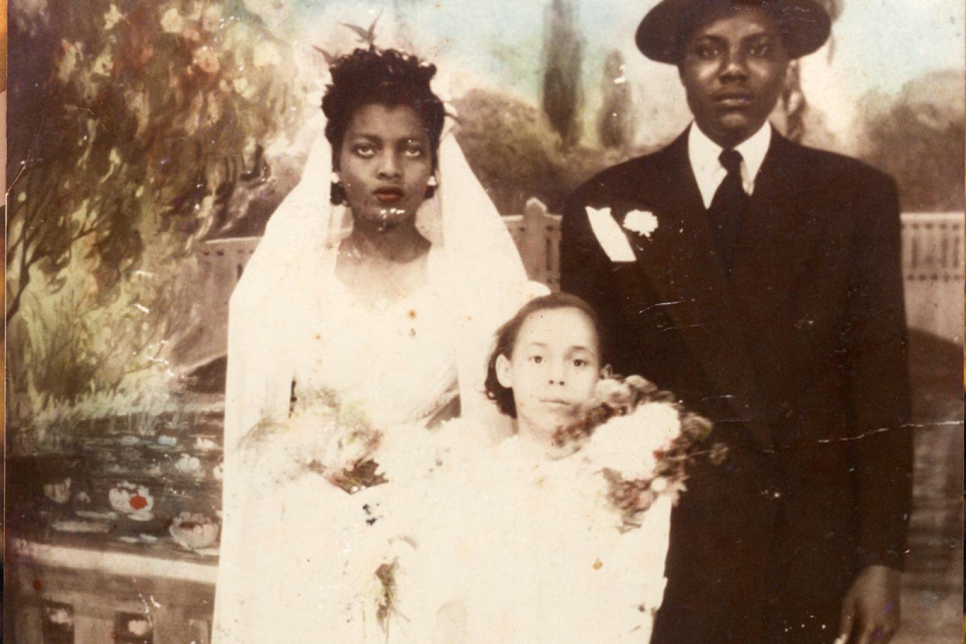 Two people wearing wedding attire with a flower girl between them.