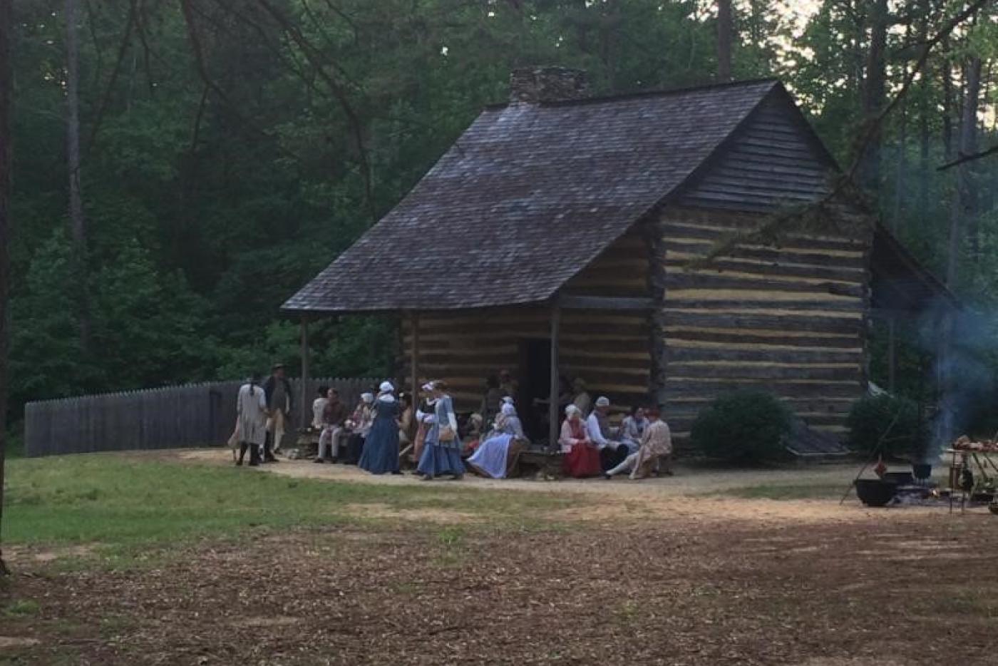 Historical interpreters outside of a large wooden cabin.