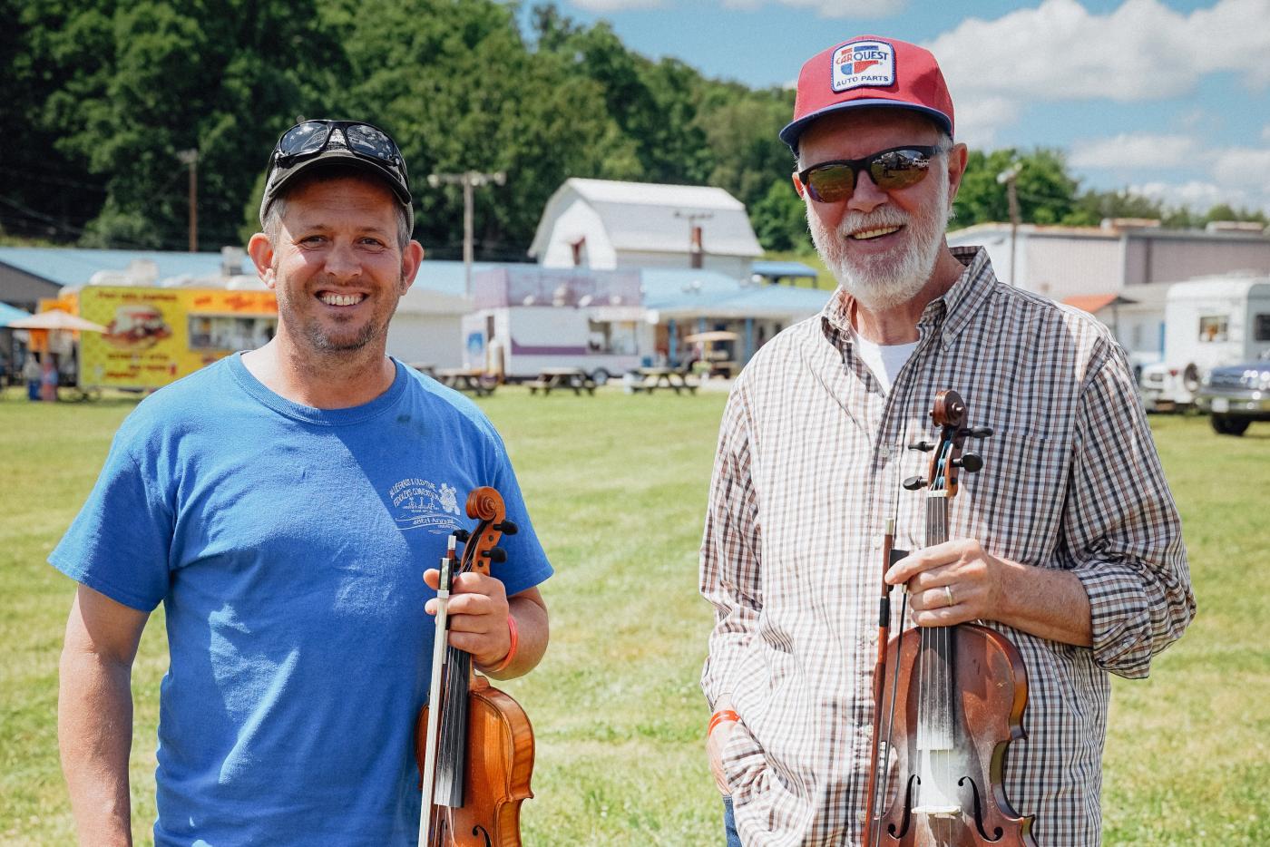 Two people holding violins outside.