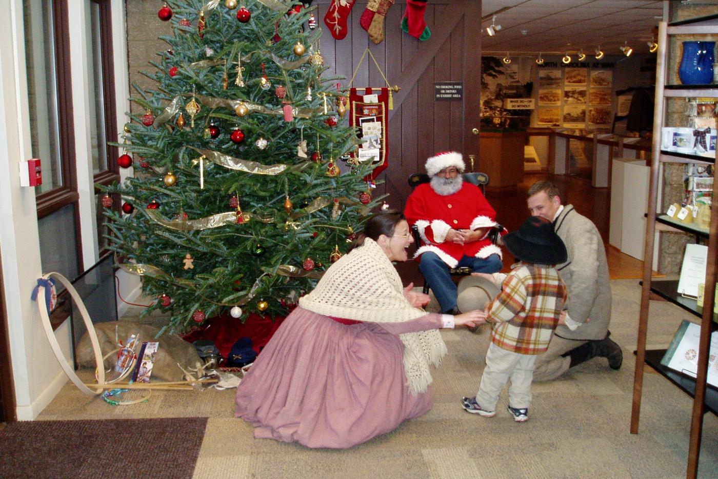 Historical interpreters greeting a child near a Christmas tree.