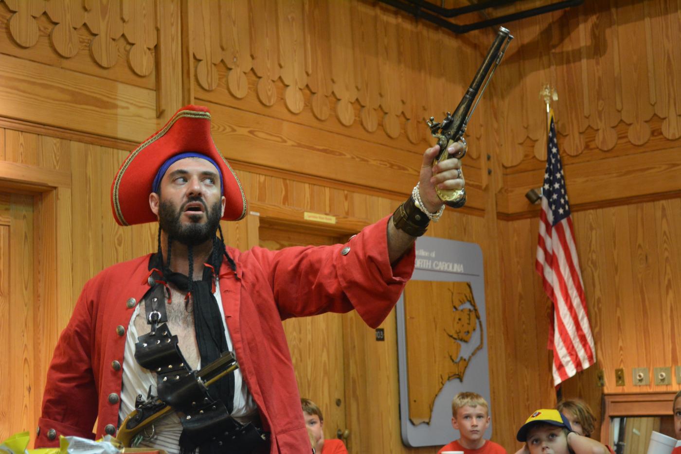 A historical interpreter dressed as a pirate holding an old revolver.