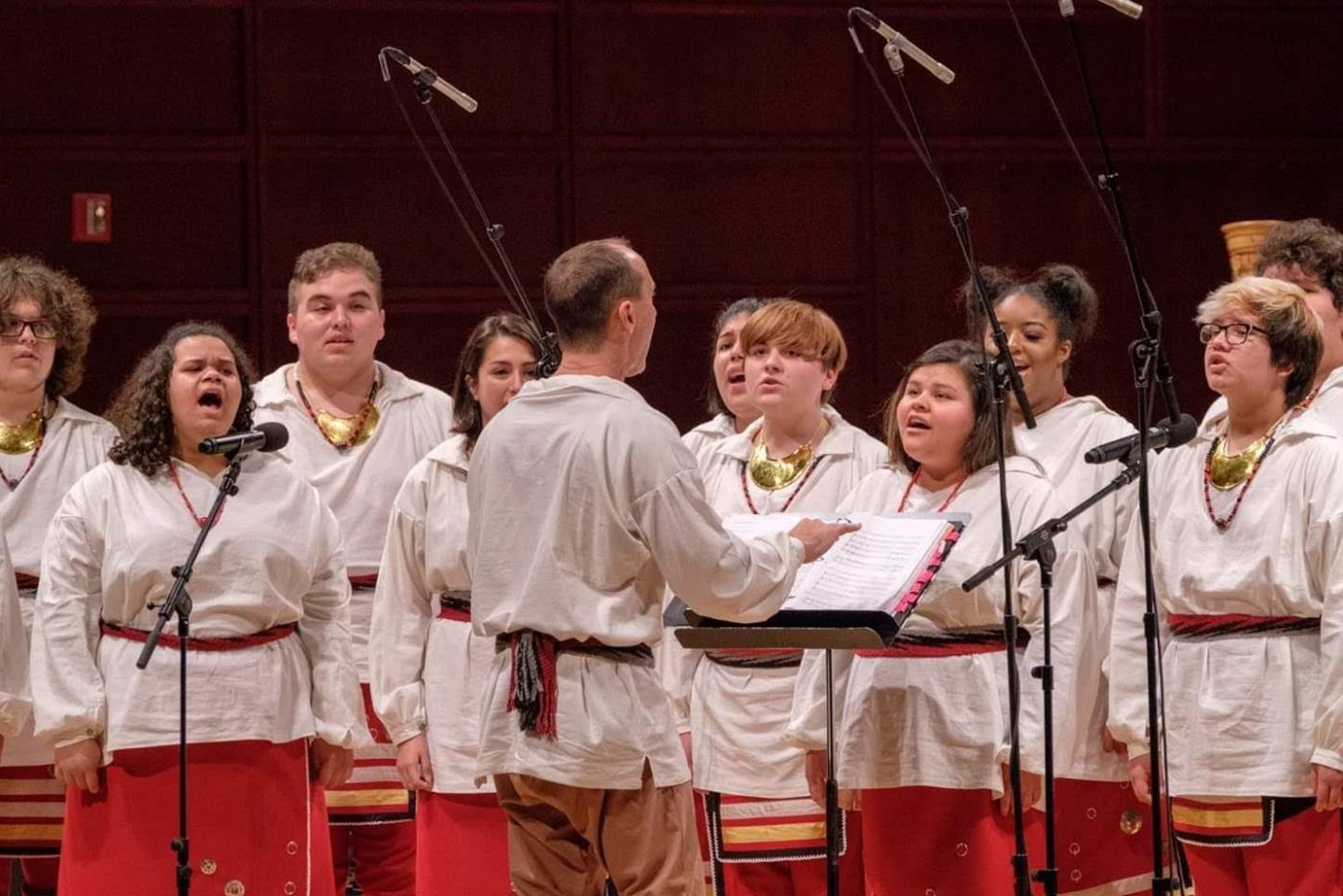 A music conductor in front of a group of singing students.