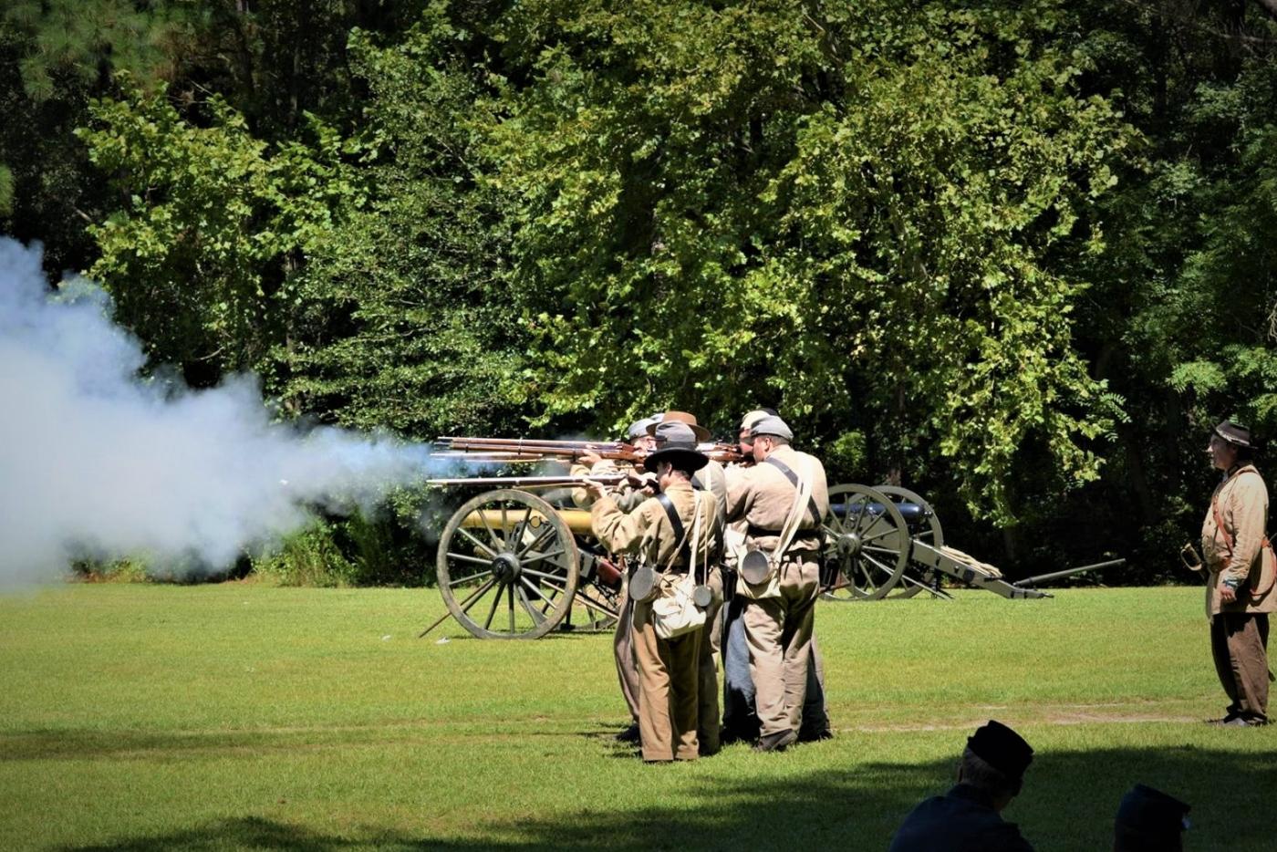Historical interpreters dressed as Civil War era soldiers, firing muskets.