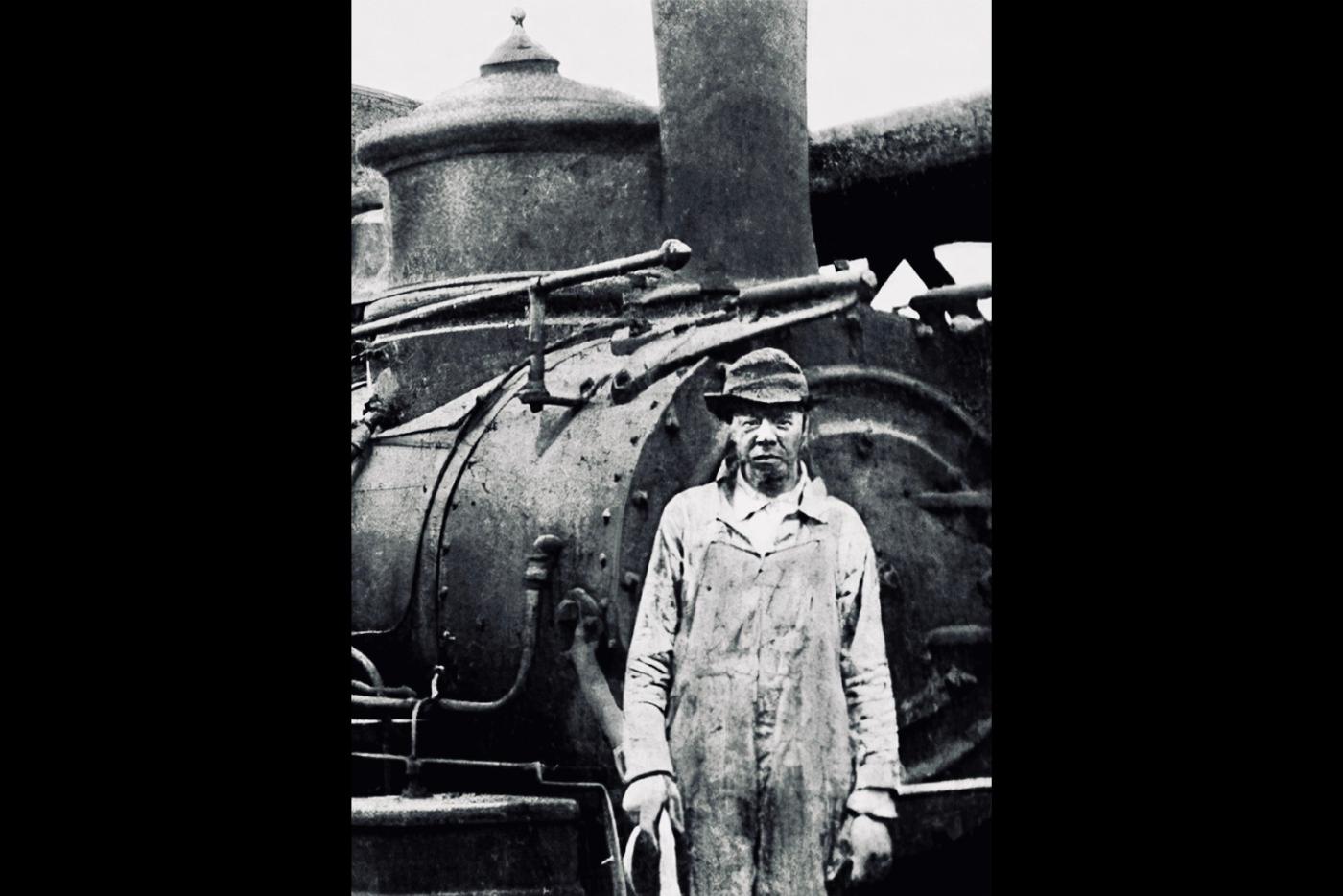 A black and white photo of a railroad worker behind a train.