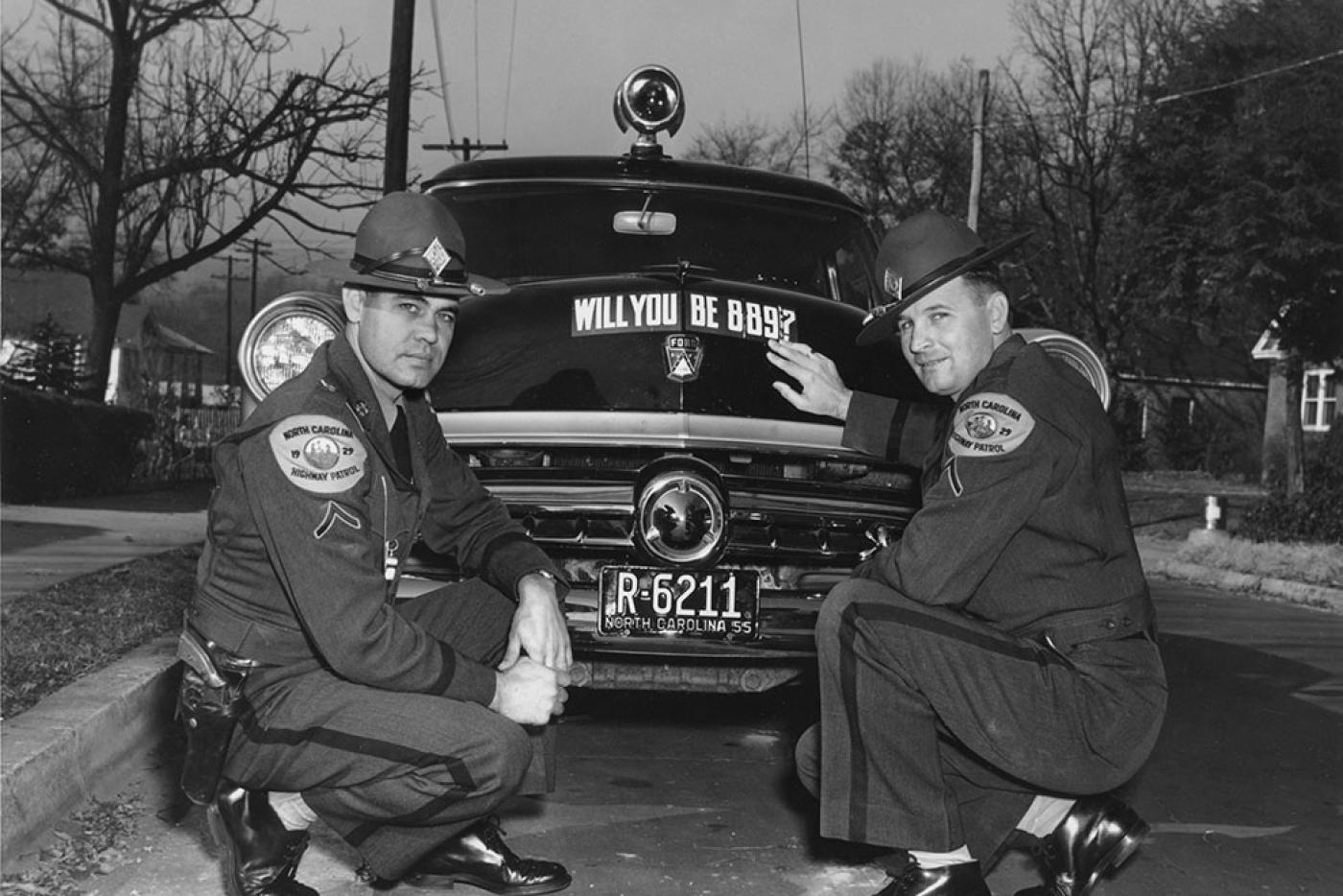 Two highway patrol officers hunched over their car.