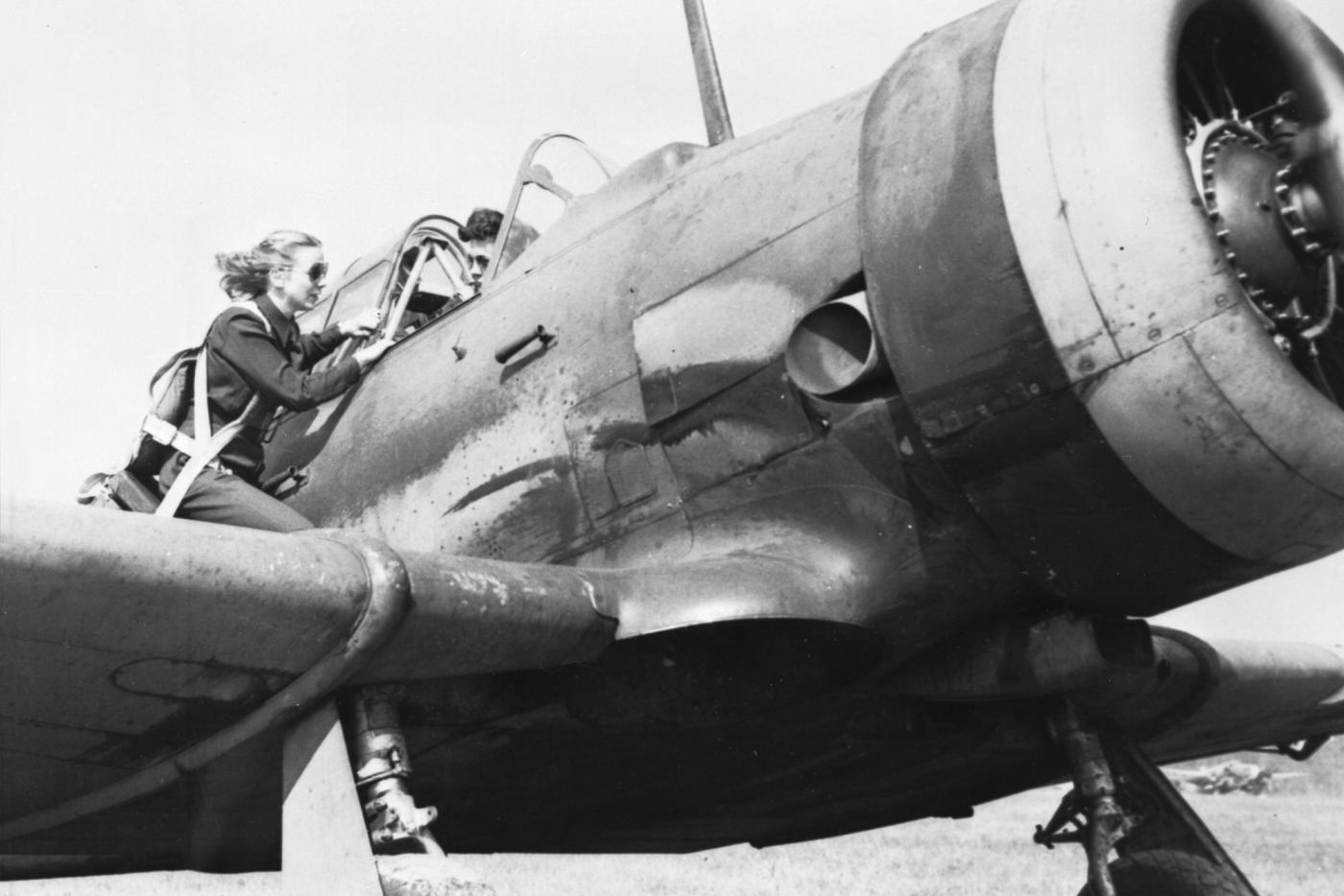 A black and white photo of a pilot entering an airplane.