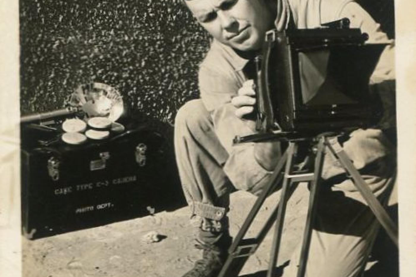 A black and white photo of a person working a 1940's camera.