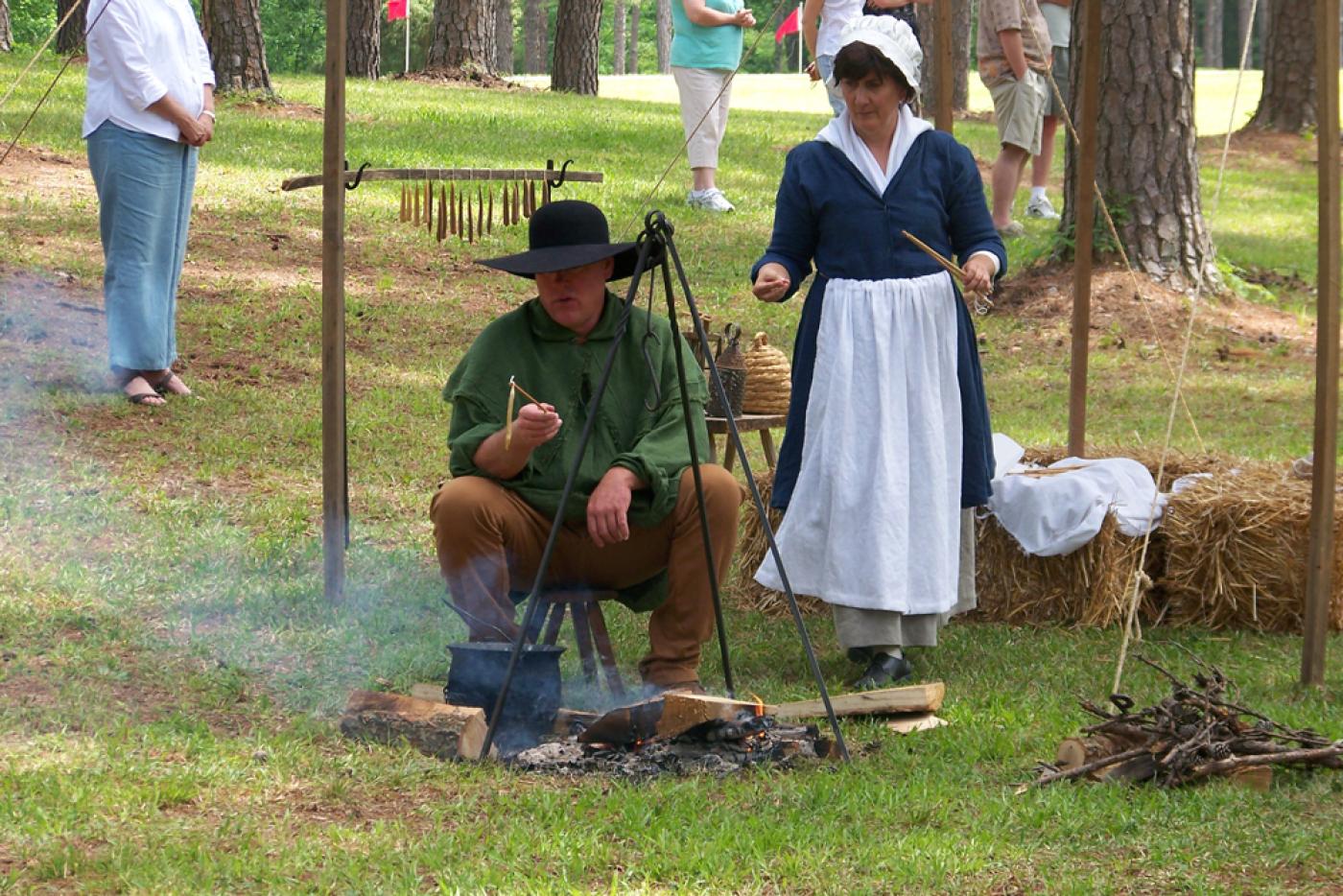 Two historical interpreters cooking a meal outside.