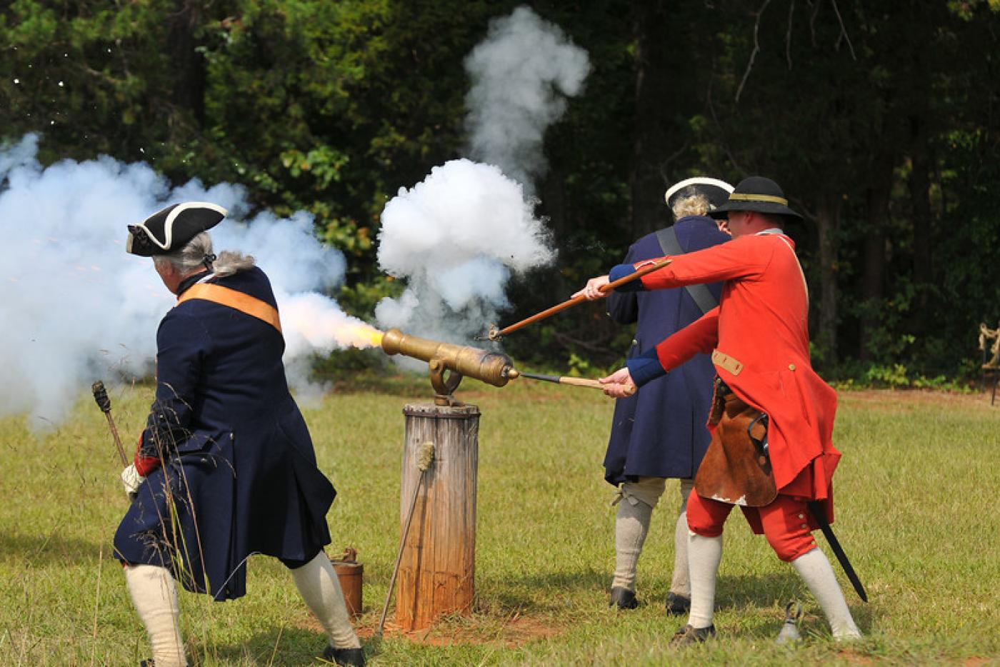Historical interpreters dressed as Revolutionary era soldiers, firing a canon.