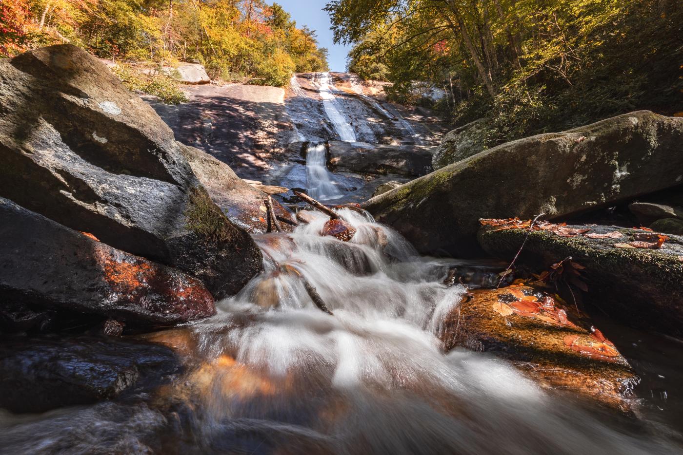 A waterfall cascade over brown rock into a pool with green trees surrounding it at Stone Mountain State Park