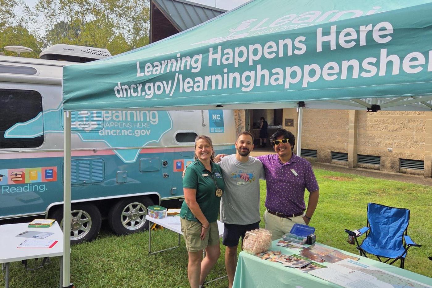 three people have their arms around each under under a teal pop up tent