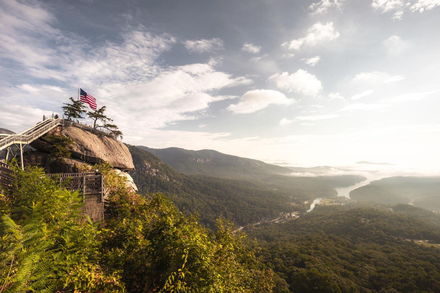 An American flag flies atop of Chimney Rock with a mountain view.