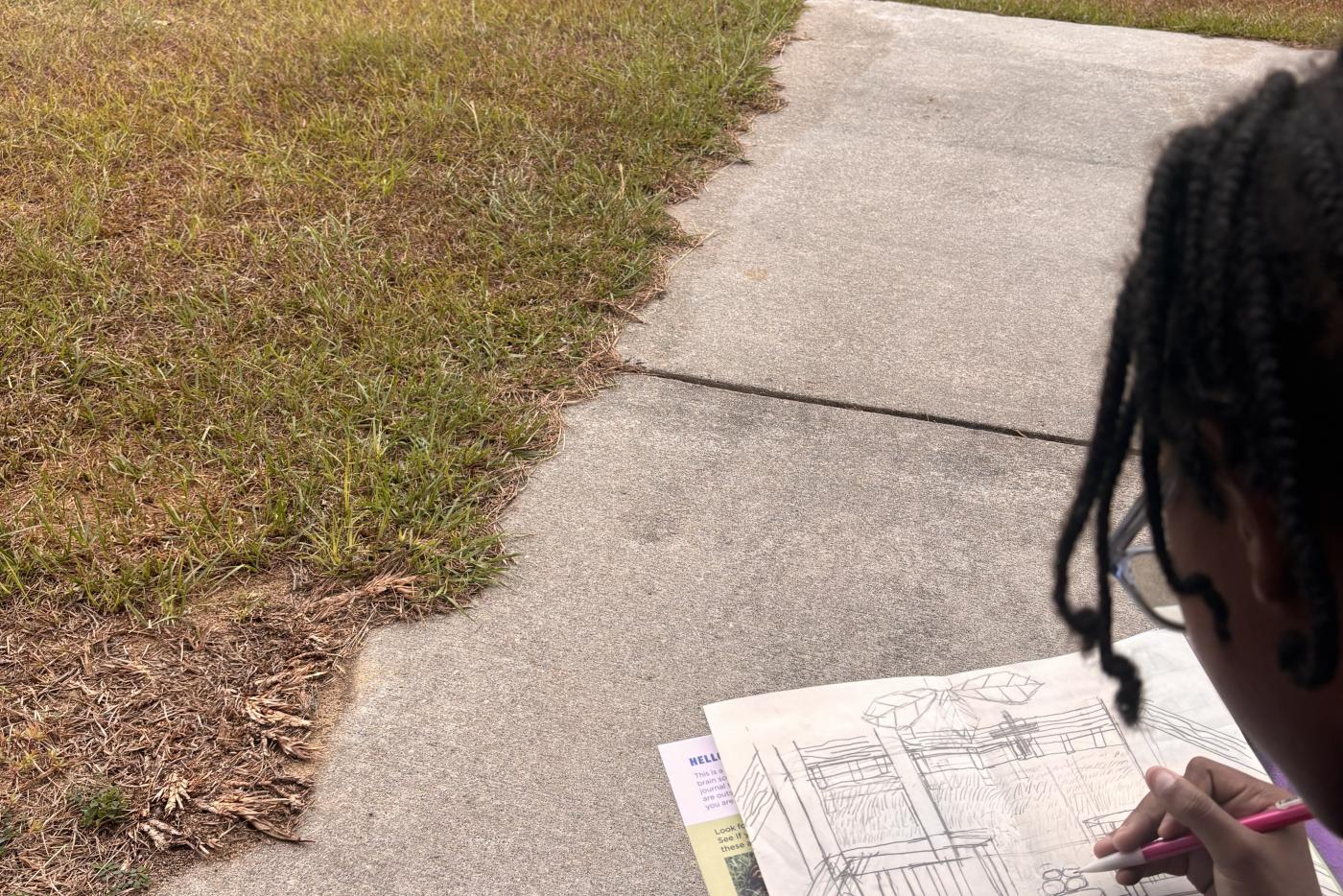 a student sits in a grassy field and journals
