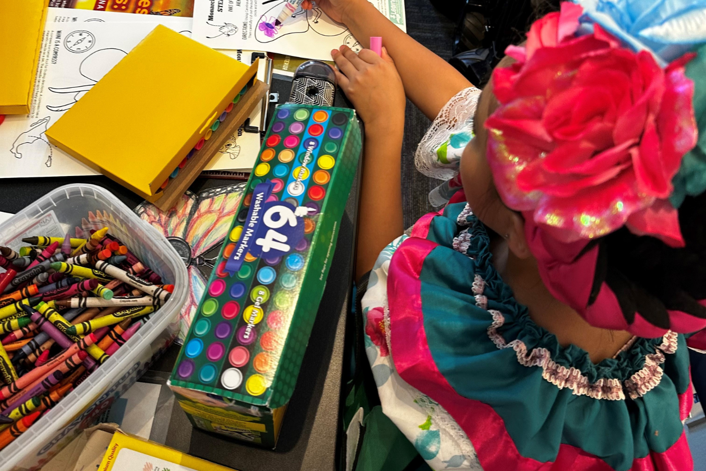 A little girl in traditional Mexican attire colors a picture.