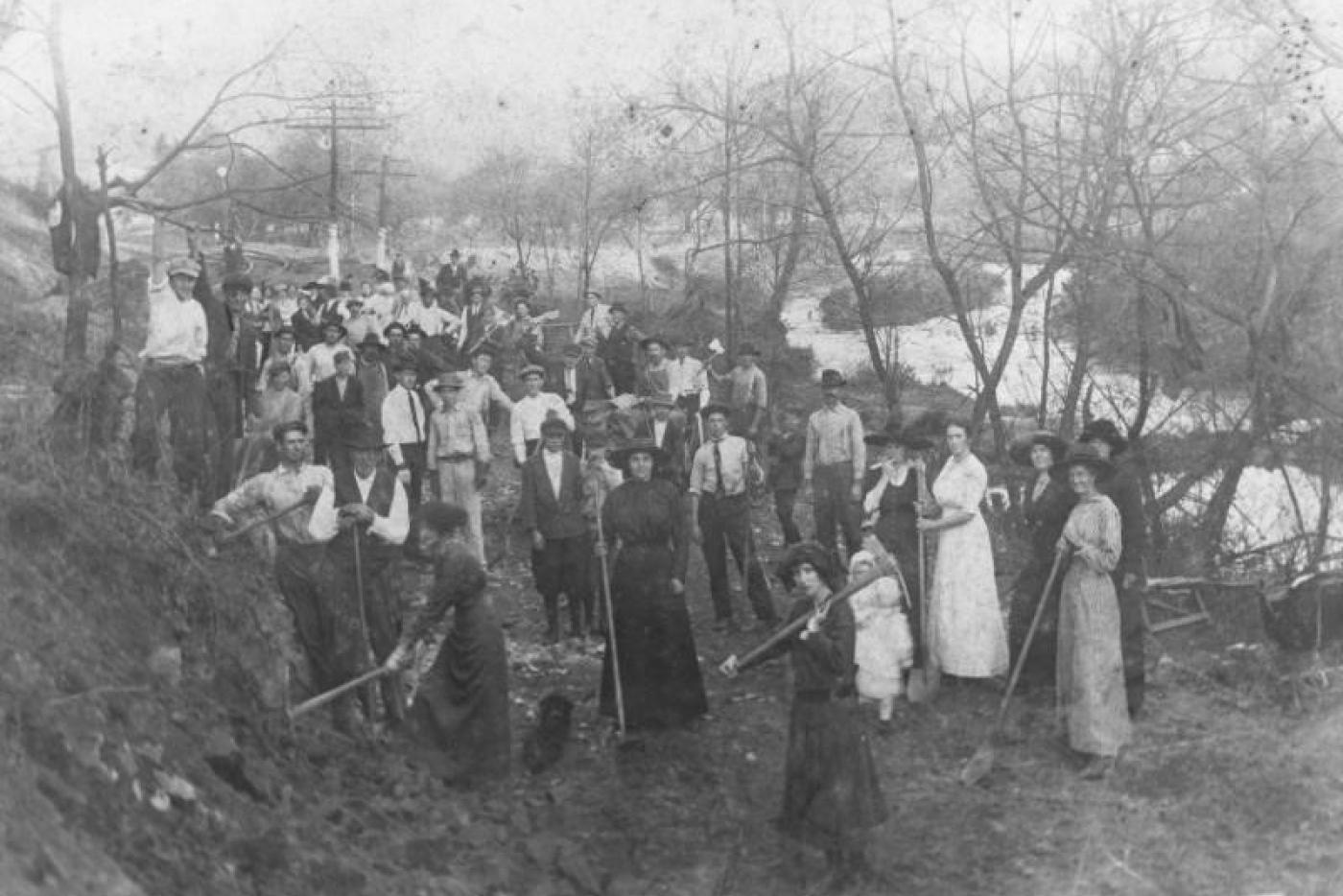 A large gathering of people holding digging equipment.