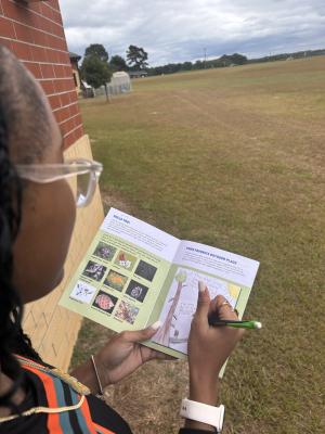 a student sits in a grassy field and journals