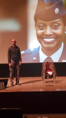 a man standing on stage with the image of a solider projected behind him