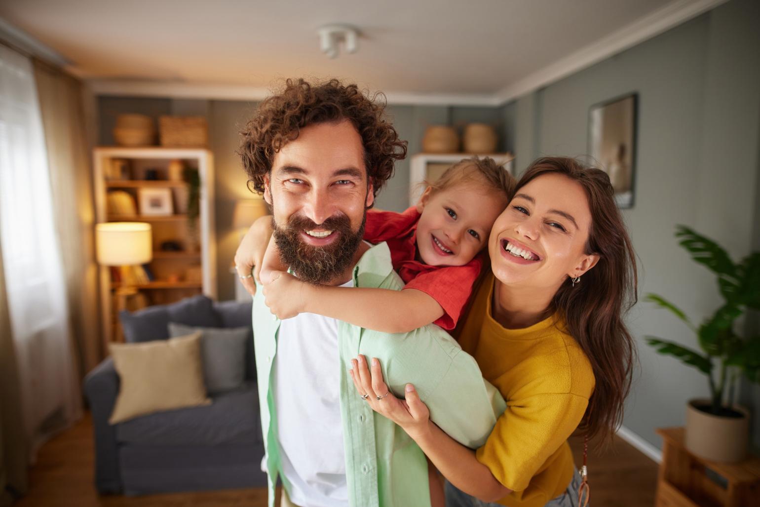 Family of three laughing and hugging, enjoying time together at home.