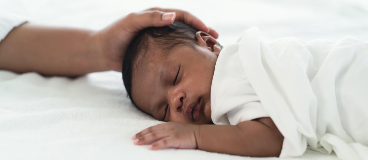 A mother rests her hand on her sleeping baby's head.