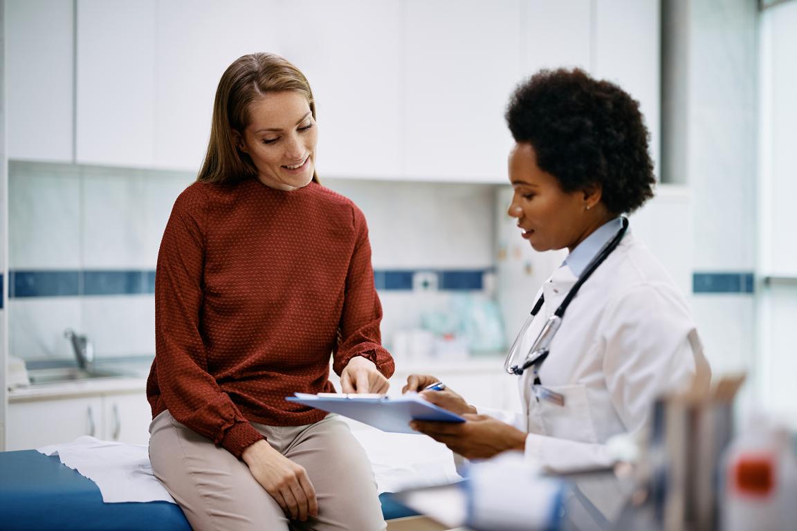 A woman sitting on an examination room table speaks with her health care provider.
