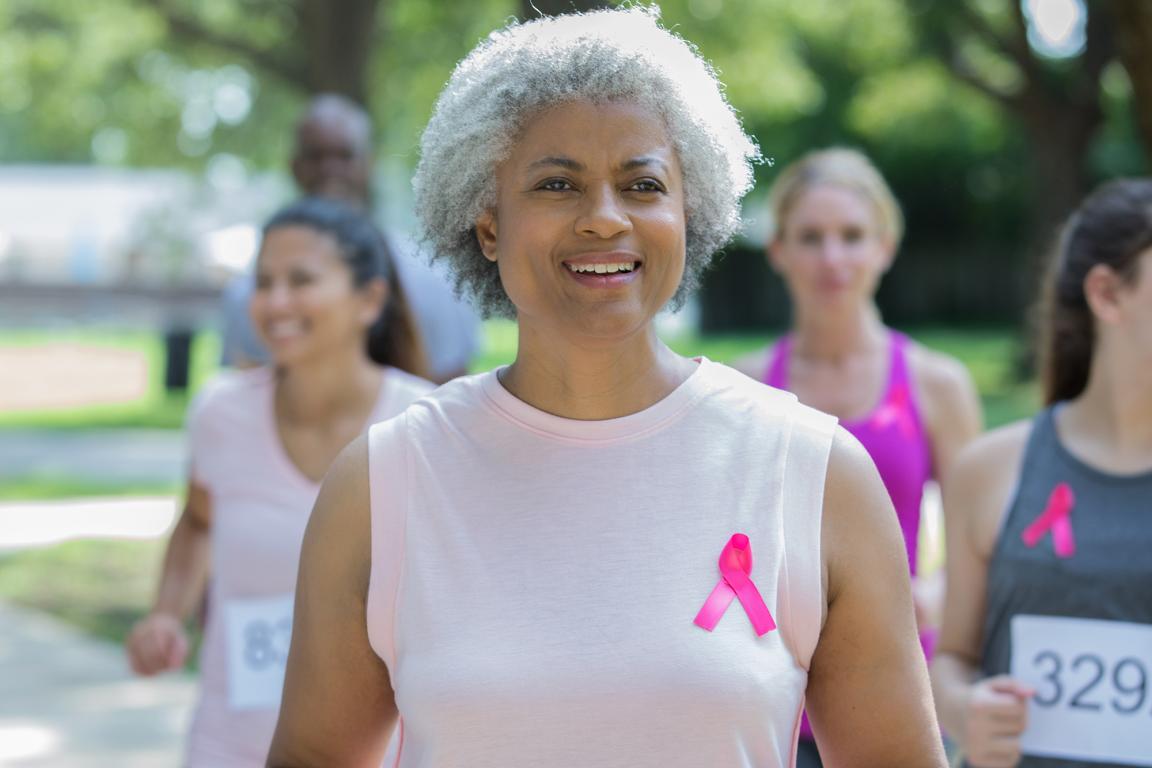 A woman with a pink ribbon on her shirt jogs during a breast cancer awareness run/walk.