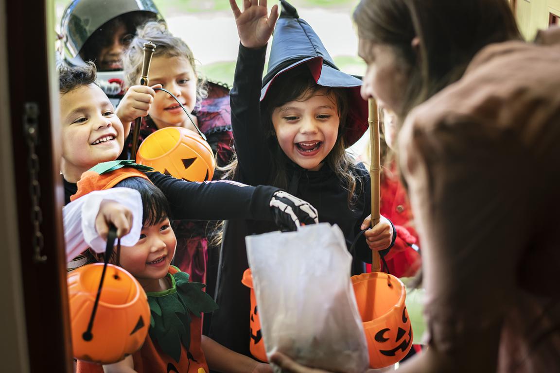 Children dressed up for Halloween trick-or-treat at a home. An adult hands out candy.