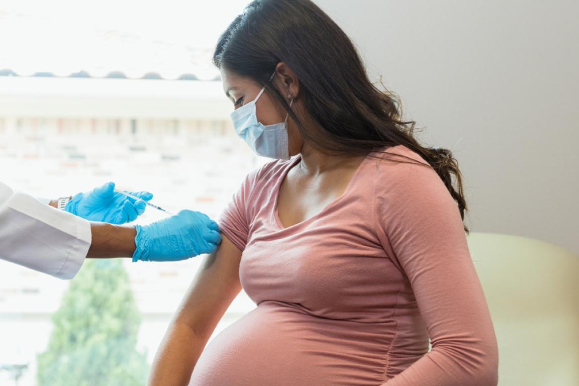 A pregnant woman receives a vaccine in a health care setting.