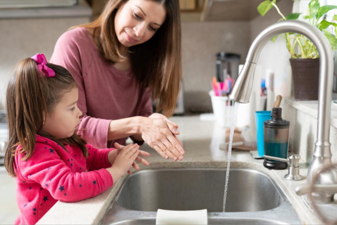 A young girl and her mother wash their hands together at the kitchen sink.