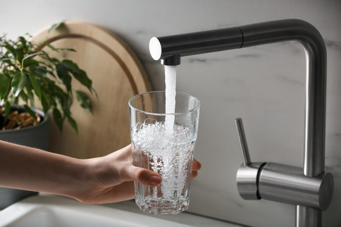 A person holds a glass of water under a running sink faucet.