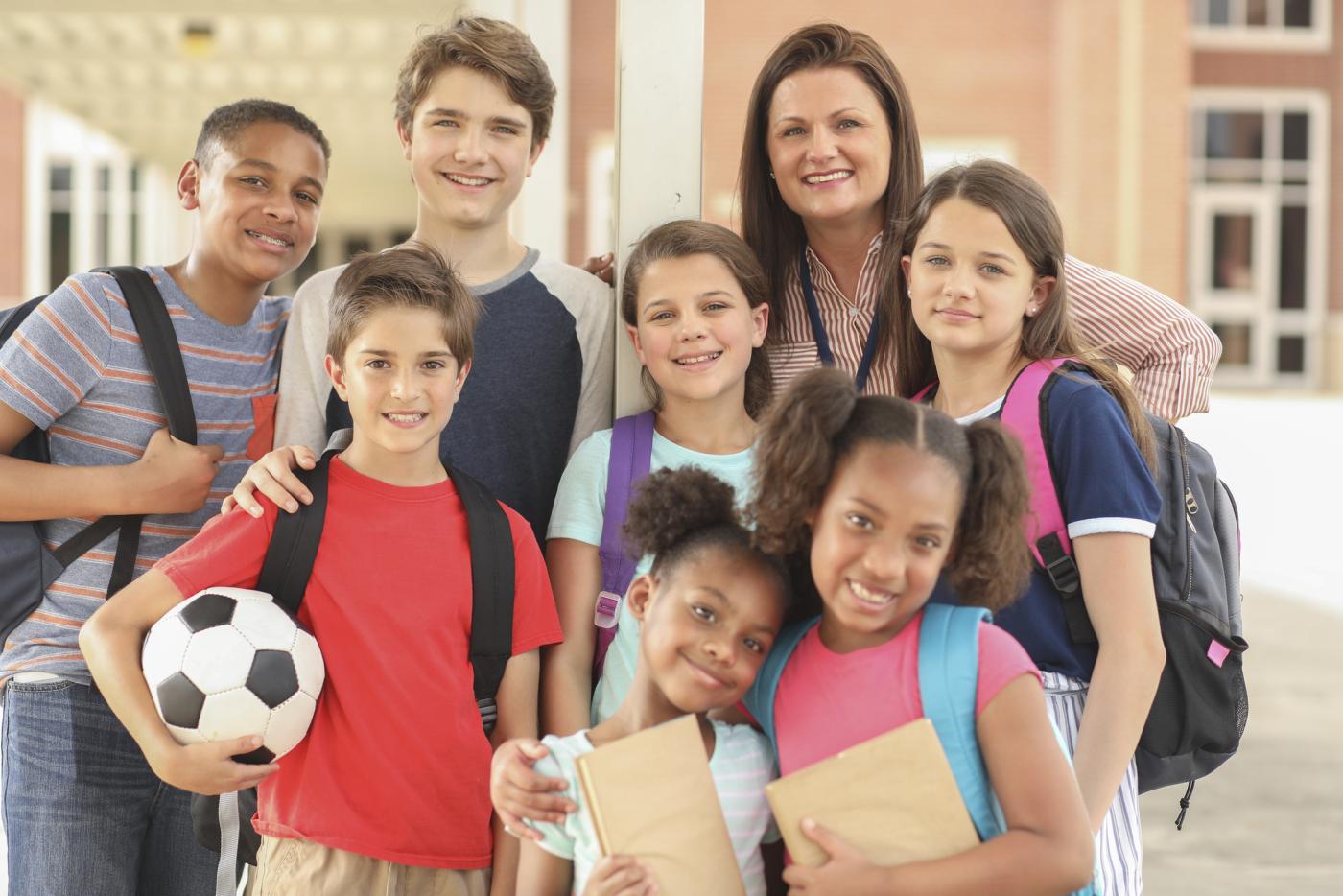 Group of children with teacher posing for photo outside school