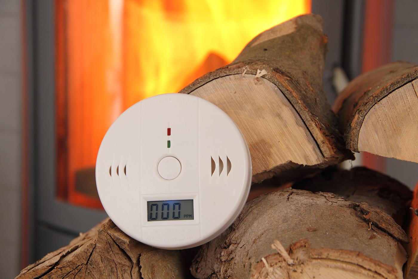 A carbon monoxide detector rests on firewood in front of a burning fireplace.