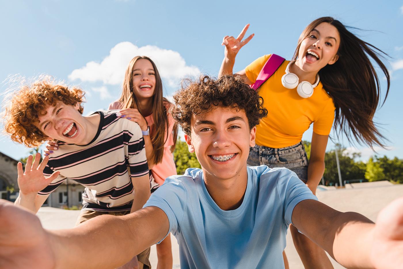 A group of teens pose for a selfie photo, with one teen holding the camera.