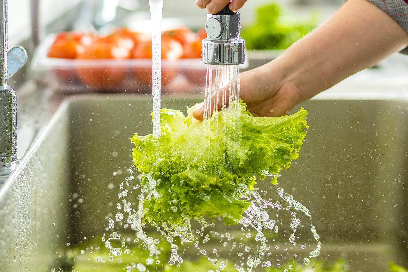 A person washes lettuce in the kitchen sink.