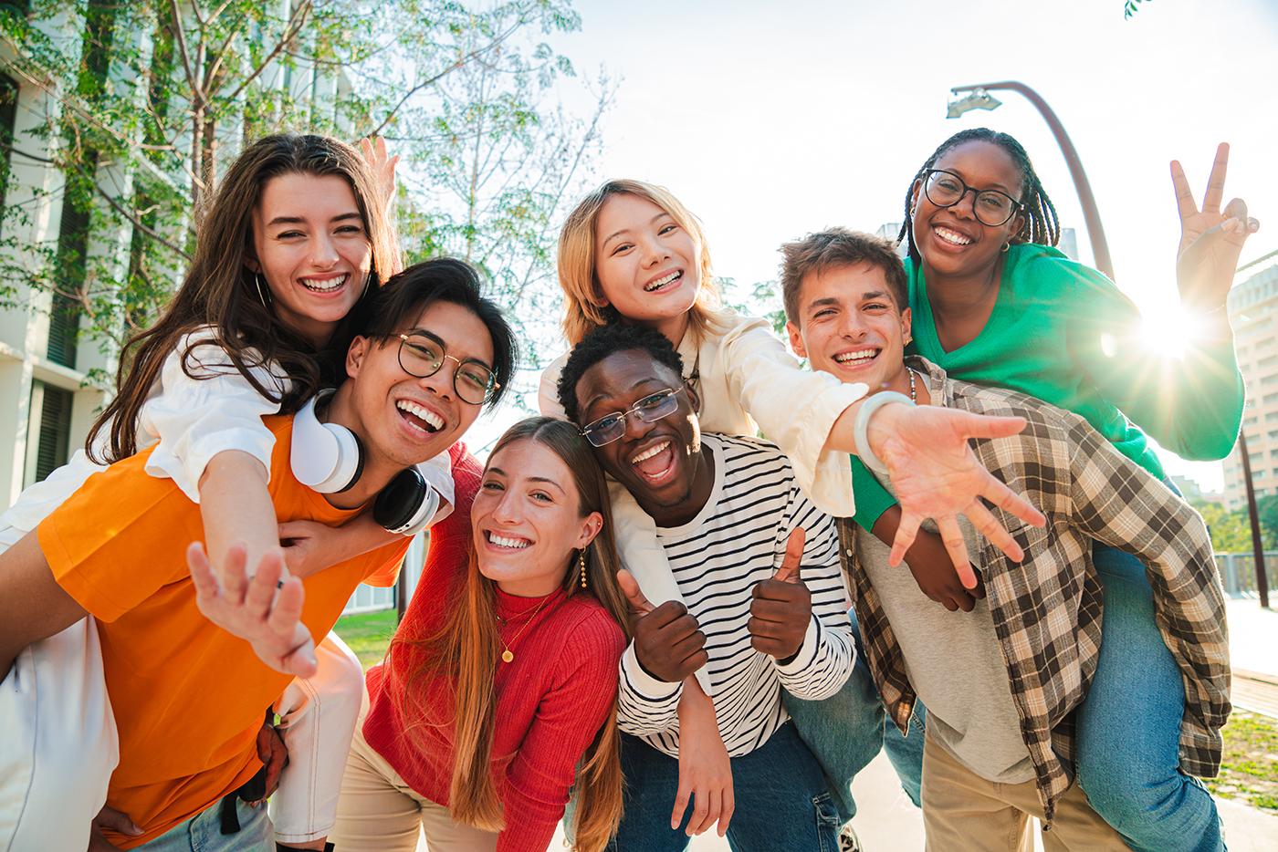 A group of seven teens smile and pose for the camera outside.