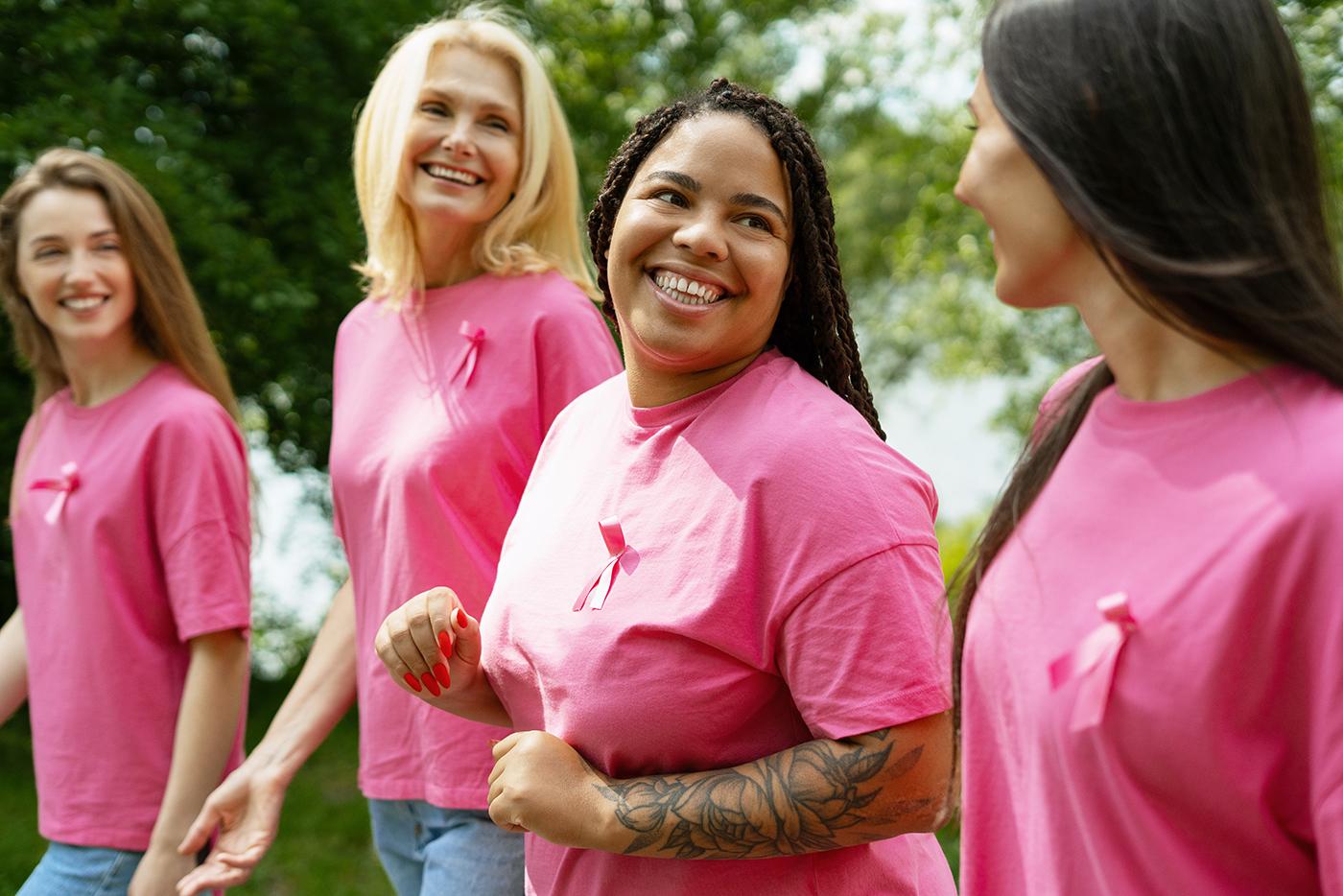 A group of four women wear pink shirts and pink ribbons during a breast cancer awareness walk.