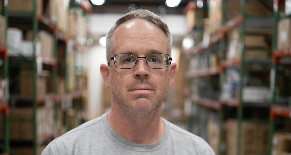 Bill stands in front of shelves of boxes in the Logistics Warehouse.