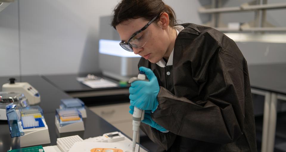Sarah wears gloves and protective eye wear while using equipment in the Sequencing and Bioinformatics Response Unit.