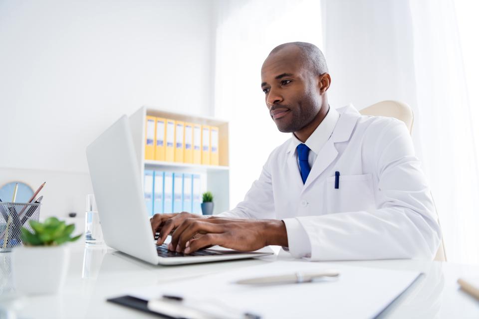 African American male doctor typing on a laptop computer. 