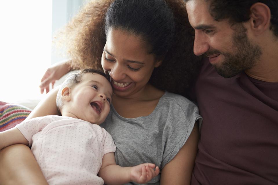 A baby sitting in her mother's lap laughs with her parents.