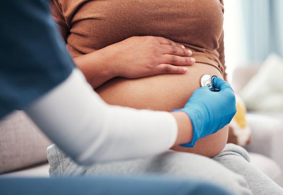 A provider uses a stethoscope on a mother's abdomen to listen to the fetal heartbeat.