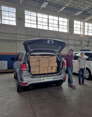 Two Division of Public Health staff members stand next to a vehicle with the back filled with supplies.