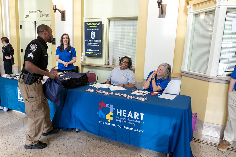 Registration table in a lobby with a blue tablecloth that has the HEART program logo on it. Three women and a man stand around table.